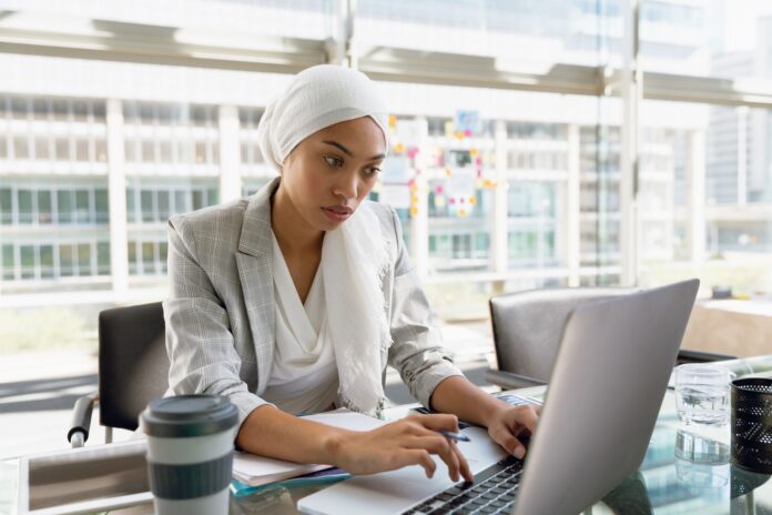 Businesswoman in hijab working on laptop at desk in a modern office